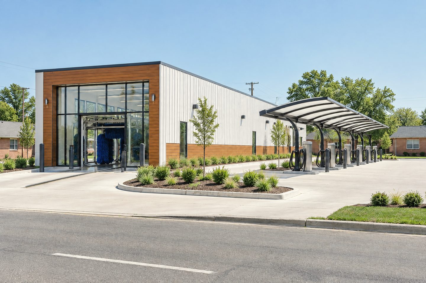 A newly built express car wash in daylight: a long white metal-panel tunnel building with a cedar-clad glass entry, an arched vacuum canopy with vacuum stations and fresh concrete lanes.