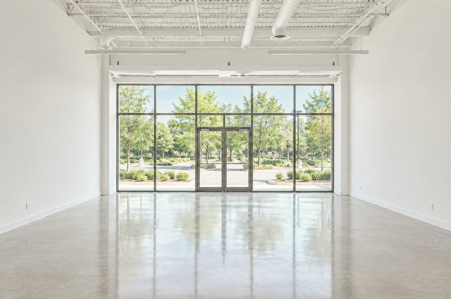 Interior of an empty, move-in-ready commercial suite: white walls, a polished concrete floor, an exposed white ceiling and a full-height storefront window wall filled with soft daylight.